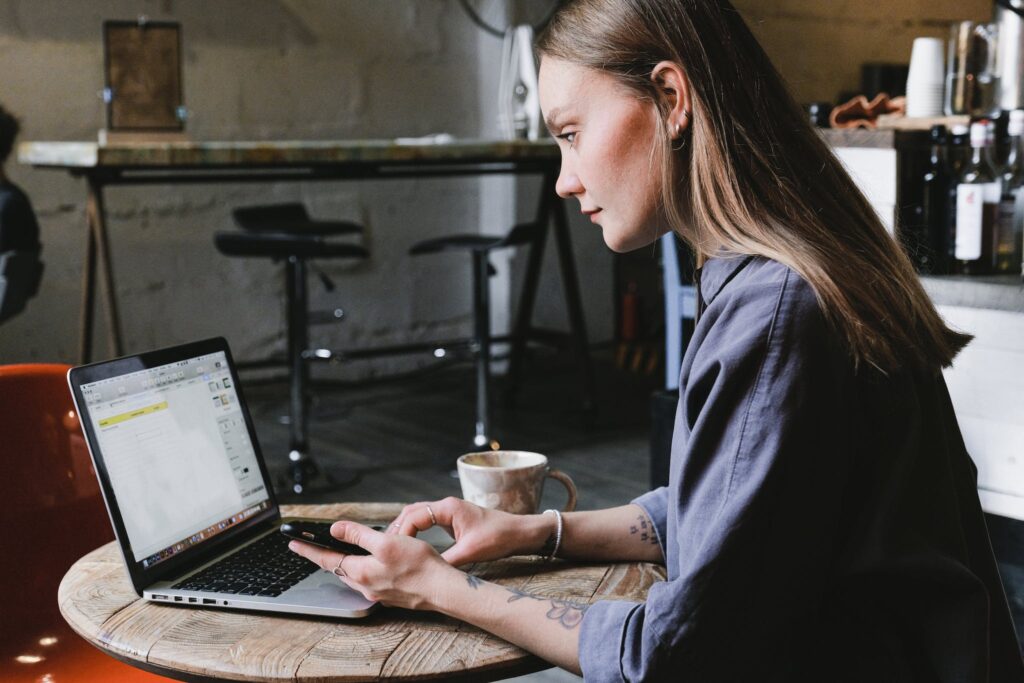 Side view of young focused woman browsing laptop sitting at table with cup of hot beverage in cafe, Best Wholesale Ecommerce Platform